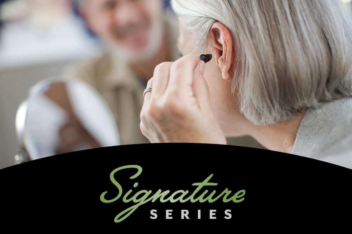 Signature Series logo, woman inserting hearing aid into ear and gentleman watching in background